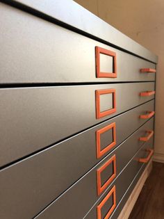 an orange and gray filing cabinet with drawers on each side, in front of a white wall