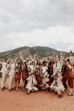 a group of people standing next to each other in front of a mountain with their hands up