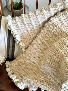 a crocheted blanket sitting on top of a wooden chair next to a potted plant