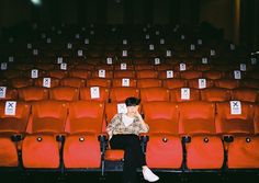 a woman sitting in an empty auditorium with her cell phone to her ear and looking at the screen