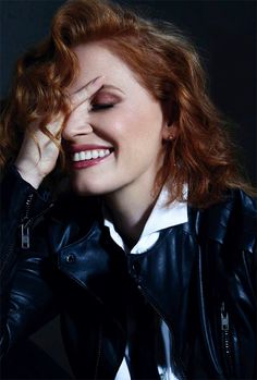 a woman with red hair smiling and wearing a black leather jacket