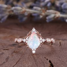 an opal and diamond ring sits on top of a piece of wood with lavender flowers in the background