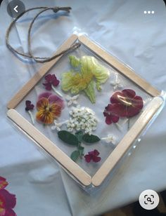 some flowers are in a glass frame on a white table cloth and there is a string attached to it