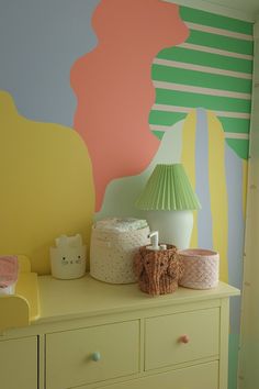 a dresser with a lamp on top of it in front of a colorful wall mural