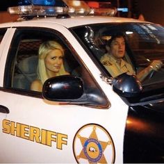 a woman sitting in the driver's seat of a police car next to a man