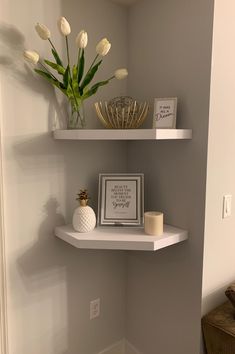 two white shelves with flowers and pictures on them in the corner of a small room