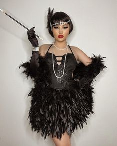 a woman dressed in black with feathers and pearls holding an umbrella while standing against a white wall