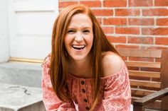 a woman with red hair sitting on a bench smiling at the camera and looking into the camera