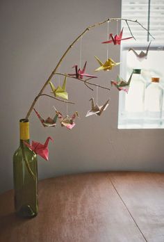 some origami birds are hanging from a branch in a wine bottle as if it were made out of paper