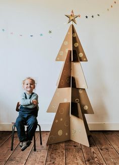 a little boy sitting in front of a cardboard christmas tree