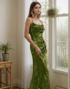 a woman standing in front of a window wearing a green sequin gown and earrings