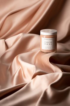 a jar of candle sitting on top of a pink satin covered bed sheet with the word coco written across it