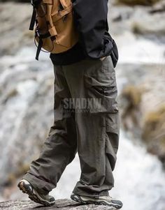 a man standing on top of a rock next to a river with a backpack over his shoulder