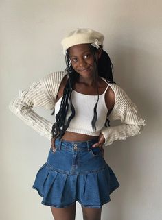 a woman wearing a white top and blue skirt with braids standing in front of a wall