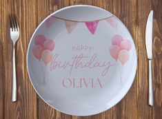 a happy birthday plate with pink balloons on it next to silverware and utensils