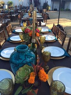 a table set with plates, vases and candlesticks for an outdoor dinner