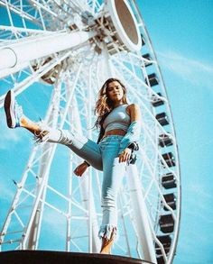 a woman standing in front of a ferris wheel with her leg up and one foot on the ground