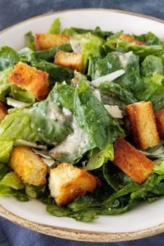 a salad with croutons and dressing in a white bowl on a blue cloth