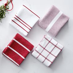 four red and white napkins sitting on top of a counter next to a sprig of rosemary