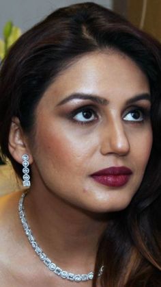 a woman wearing a necklace and earrings with diamonds on her neck, posing for the camera