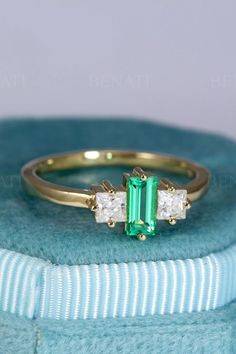 an emerald and diamond ring sitting on top of a blue box