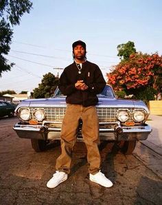 a man standing in front of a car on the side of the road with his hands crossed