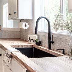 a kitchen with white cabinets and wood counter tops, black faucet, and wooden counters