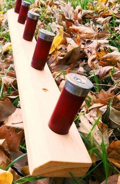 three red cups sitting on top of a wooden bench in the grass with leaves around them