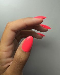 a woman's hand with bright pink nail polish on her nails, against a gray background