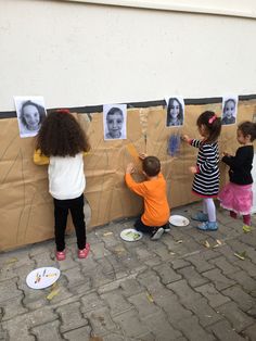 three children are playing with pictures on a bulletin board that is taped to the wall