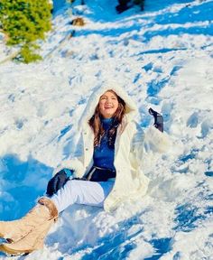 a young woman sitting in the snow with her feet up and arms out, smiling at the camera