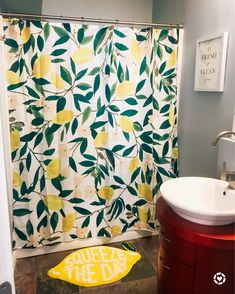 a bathroom with a shower curtain, sink and yellow lemons on the shower mat