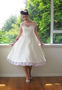 a woman standing in front of a window wearing a white dress with polka dots on it