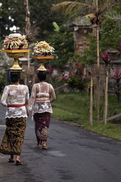 two women are walking down the street carrying vases on their heads and baskets on their heads