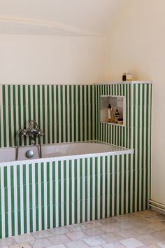 a bathroom with green and white striped tiles on the walls, tub and shower head