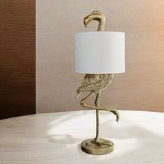 a gold flamingo lamp sitting on top of a table next to a white shade