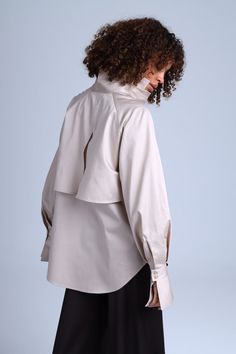 The beige caped shirt Diva is a unique creation that blends classic elegance with a modern twist. This button-down shirt features a cape-like design that gracefully drapes over the shoulders and back, creating a stunning winged effect. The puffy long sleeves with bell-shaped cuffs add a touch of refinement to this exquisite piece. Crafted from premium cotton satin, the Diva Beige shirt is not only luxurious but also comfortable to wear all day long. Its adaptable design allows you to experiment with different bottom options, enabling you to create a one-of-a-kind ensemble that reflects your personal style. Elegant Cape Top For Spring, Elegant Spring Cape Top, Chic Neutral Fall Shirt, Elegant Neutral Shirt For Spring, Elegant Oversized Beige Tops, Elegant Collared Blouse In Neutral Color, Puffy Long Sleeves, Beige Shirt, The Diva