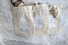 two bags with christmas trees on them are sitting on a white blanket and one has a chocolate bar in it