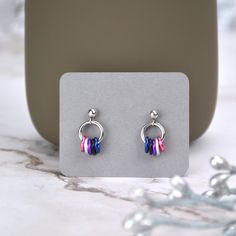 a pair of colorful earrings sitting on top of a white table next to a silver object