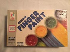 a box of finger paint sitting on top of a white tablecloth covered floor next to a cat