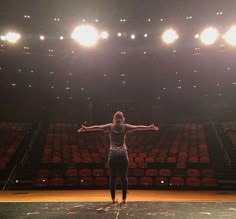 a woman standing on top of a basketball court in front of an empty stadium filled with red seats