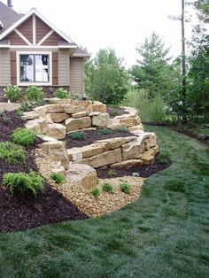 a stone wall in front of a house with landscaping around it and grass on the ground