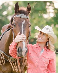 a woman standing next to a horse wearing a cowboy hat and holding the bridle