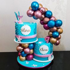 three tiered cake decorated with balloons and nameplates on each layer, sitting on top of a black table