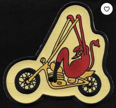 an embroidered patch with a cartoon character on a motorbike in the shape of a letter