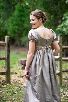 a woman in a dress is walking through the grass with her hand on her hip