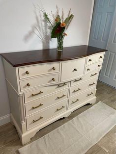 a white dresser with drawers and flowers in a vase on it's top shelf