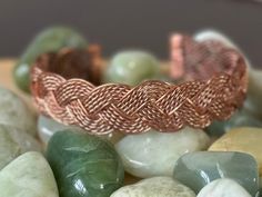 a close up of a bracelet on top of some rocks and green glass stones with gold wire