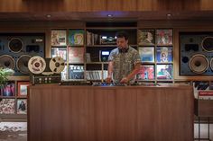 a man standing behind a wooden counter in a room with record players on the walls