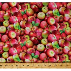 a large pile of red apples with green leaves on them, in front of a ruler